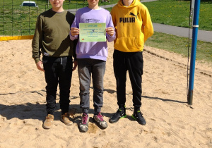 Trzech chłopców stoi na boisku z dyplomem